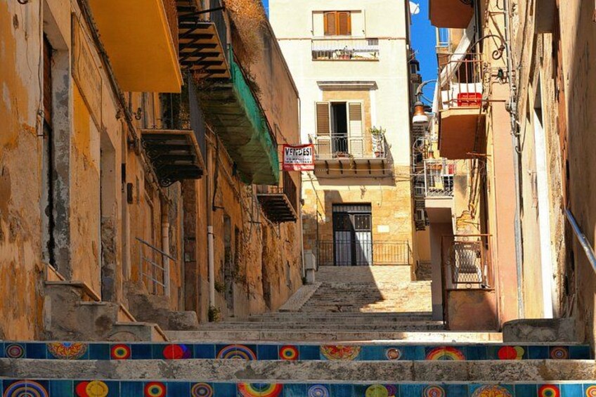 A narrow street with buildings, a visible sign, and colorful tiled steps. 2