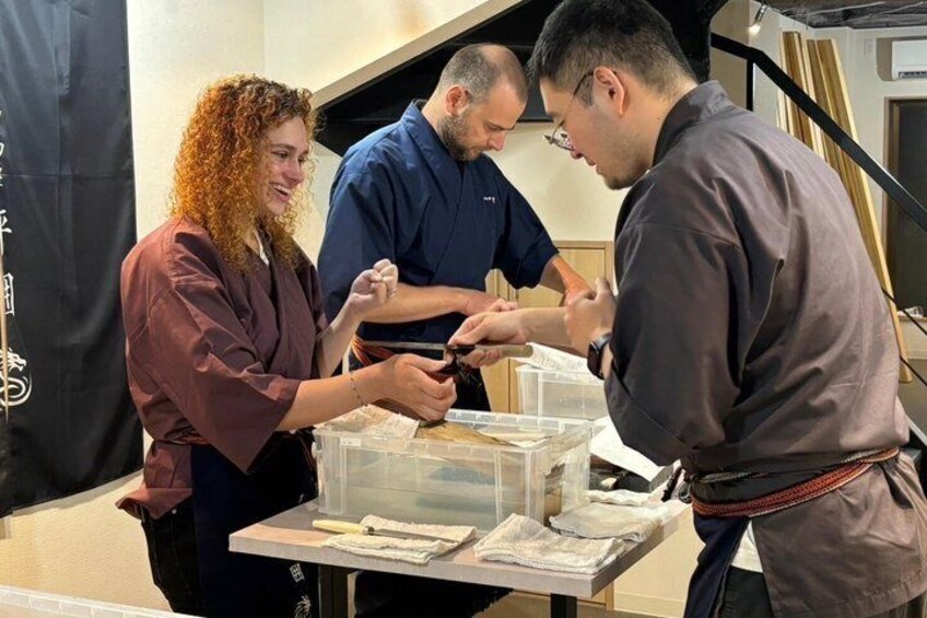 Trois personnes sont assises à une table devant un récipient transparent, probablement dans un atelier ou un bureau. 1