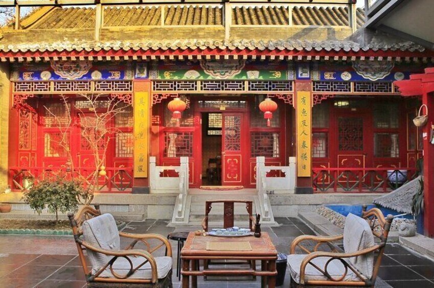 A traditional Chinese building with red and yellow decorations, a tiled roof, and a table with chairs in front. 4
