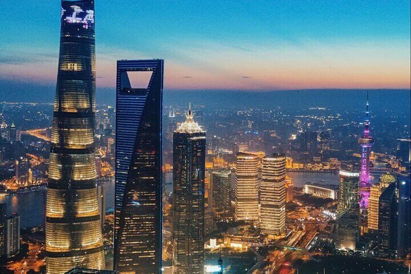 A cityscape with illuminated skyscrapers, including a distinctive tower with a spire and a building with a unique angular design. 1