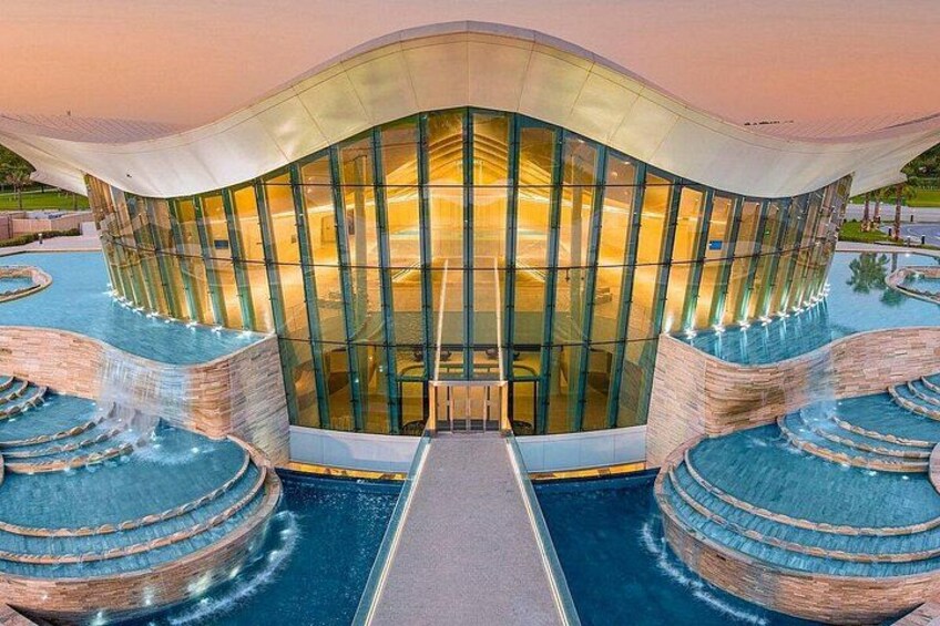 A modern building with a glass facade and a pool with a waterfall feature. 1