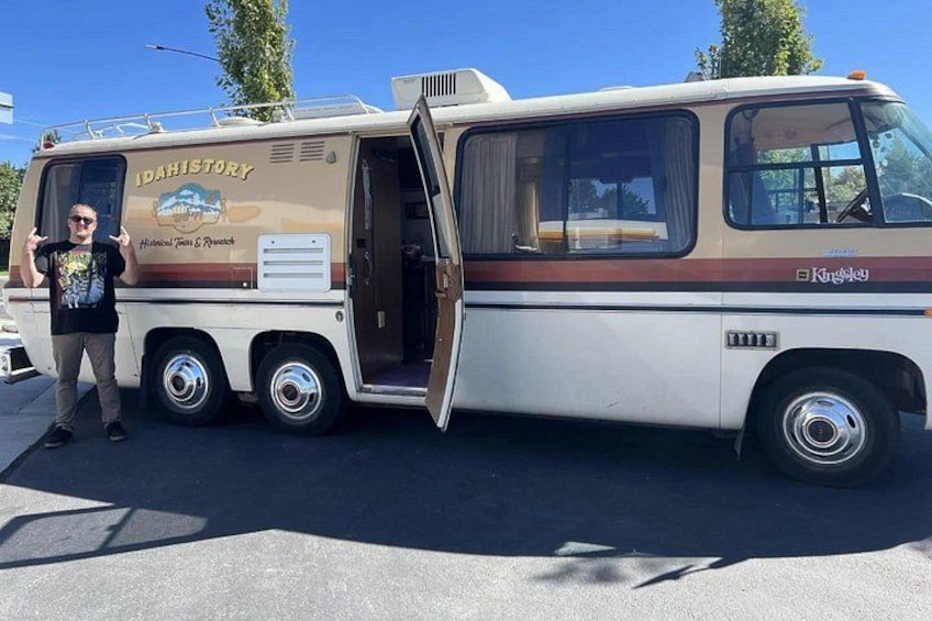 A vintage bus with the text 'Idahistory' on its side, parked in a lot. 1