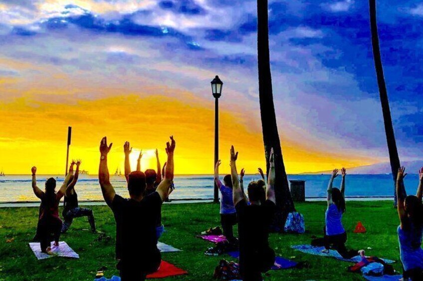 People doing yoga on mats on a grassy field by the water during sunset. 1