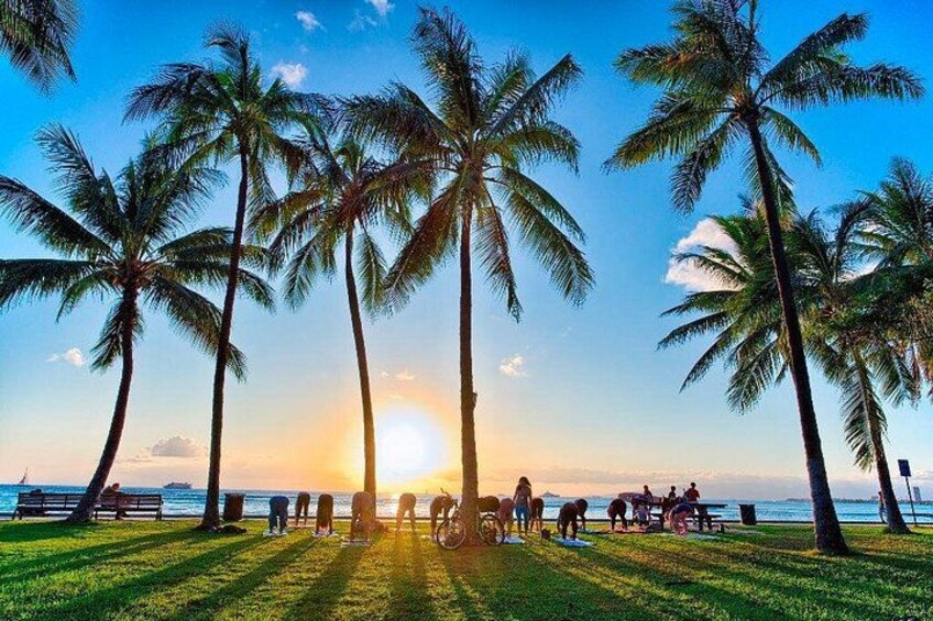 Una playa al atardecer con palmeras, gente caminando y una bicicleta. 3
