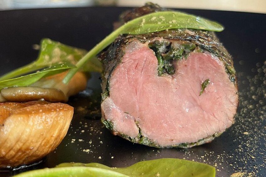 A sliced piece of meat with a pink center, surrounded by green leaves and mushrooms on a dark plate. 3