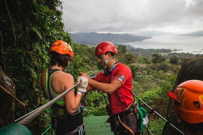 Two people in helmets and harnesses on a rope course with a view of a lake and mountains in the background. 1