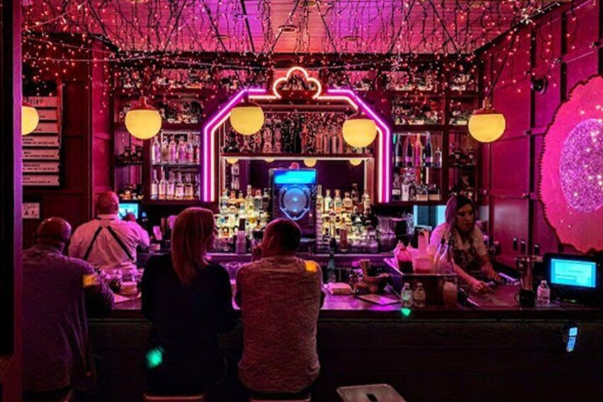 Un bar con luces de neón, botellas y gente. 5