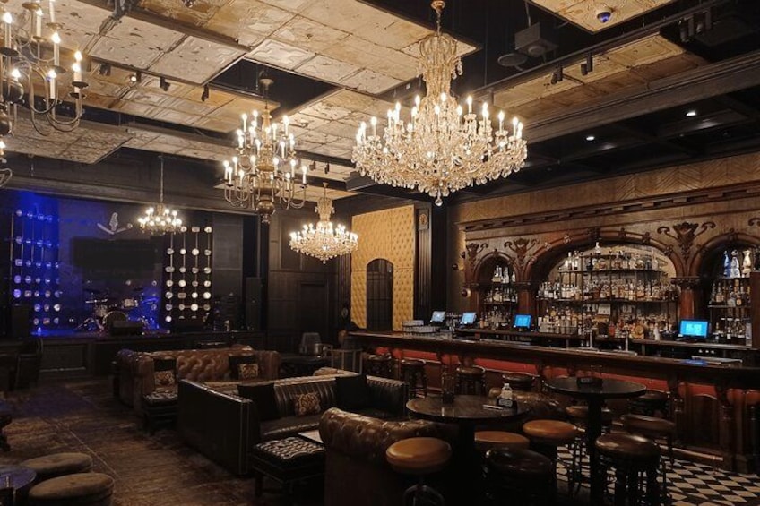 Un bar con asientos de cuero, candelabros y un escenario con músicos. 4