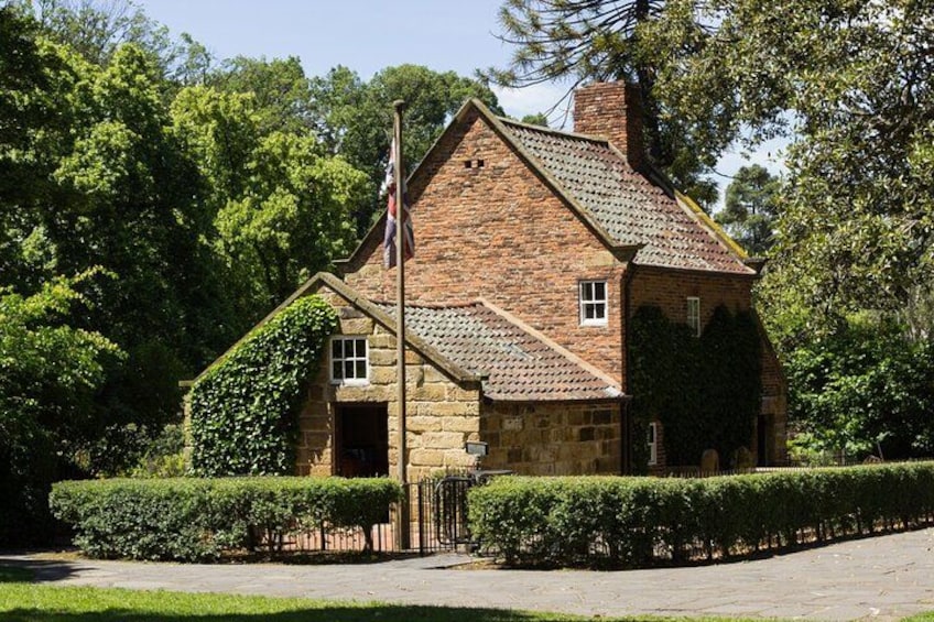 A stone house with a tiled roof, surrounded by greenery and a hedge. 3