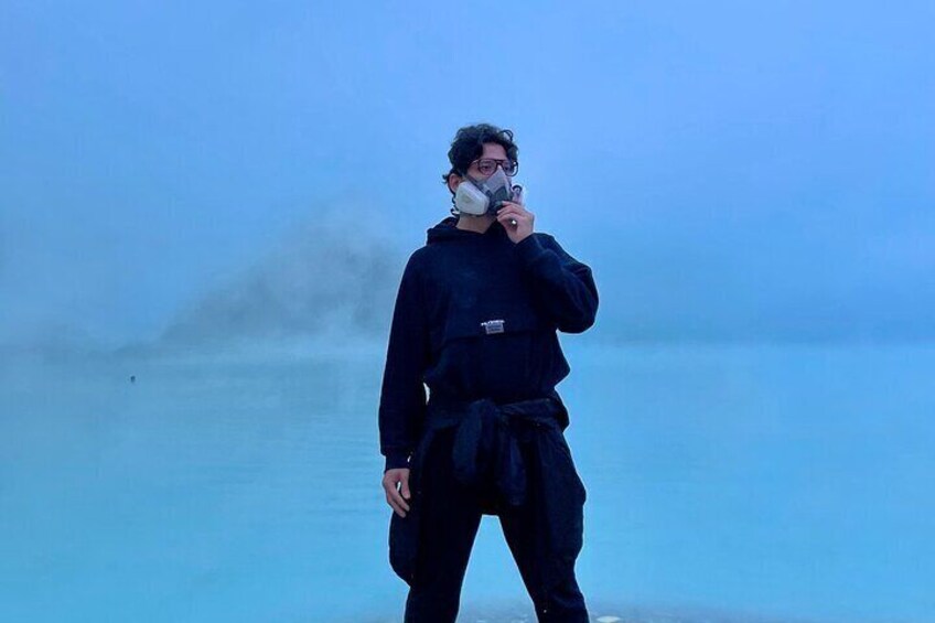 A person in black attire standing on a beach with a blue sky and mist in the background. 2