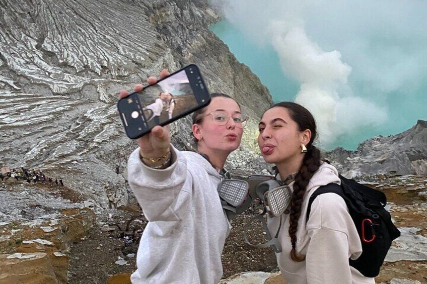 Two people taking a selfie with a smartphone in a mountainous area with visible rock formations and a body of water. 4