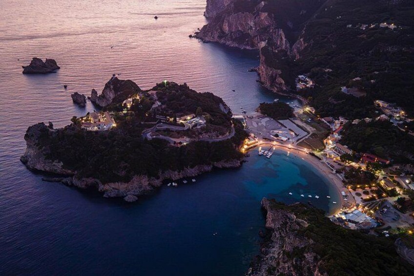Un pueblo costero al atardecer con edificios iluminados, un puerto deportivo y acantilados rocosos. 2