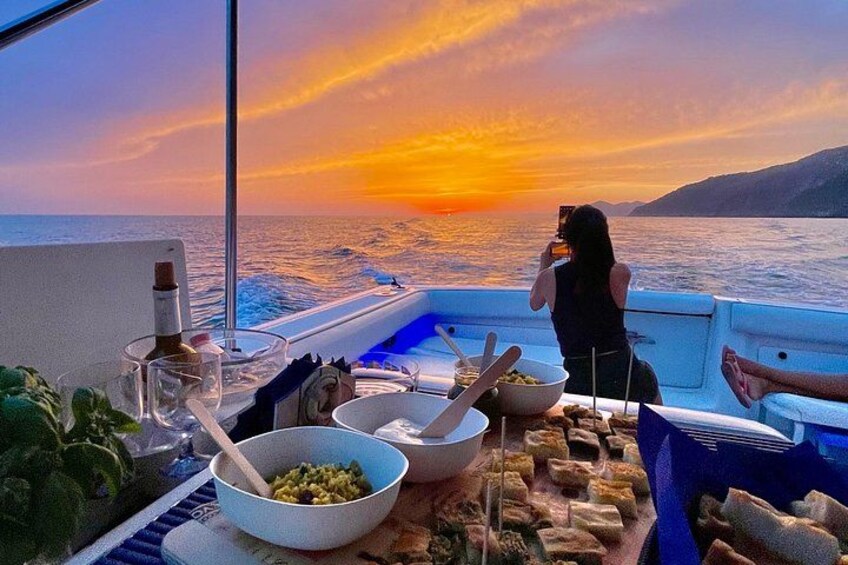 A boat with a sunset view, bowls of food, and a person taking a photo. 1