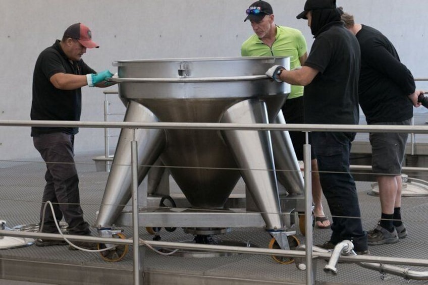 Cuatro personas operando una máquina industrial grande con forma de embudo sobre una plataforma metálica. 5