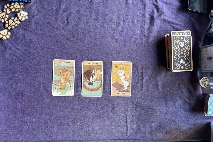 Tre tarotkort på et lilla klæde med et lommeur og en spillekortæske. 2