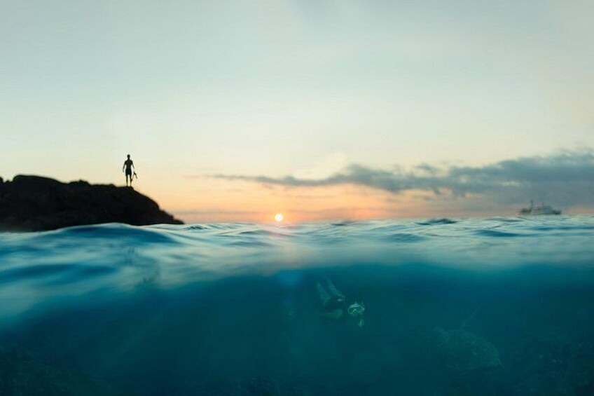 A person standing on a rock with a boat in the water and a sunset in the background. 2