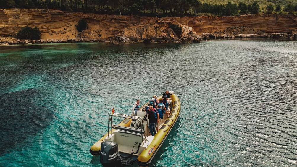 Un bateau gonflable jaune, avec des personnes à bord, flottant sur une eau claire près d’une côte rocheuse. 5