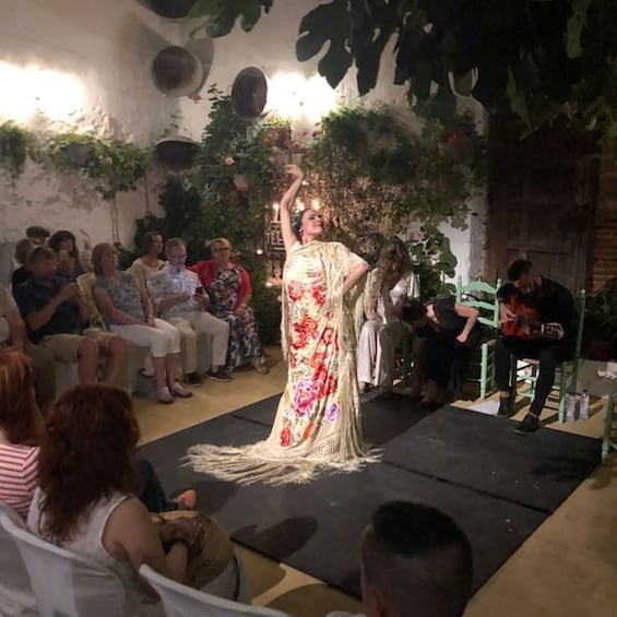 A person in a floral dress performing on a stage with an audience seated in chairs. 5