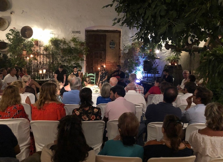 A group of people seated at tables, facing a stage with musicians performing. 3