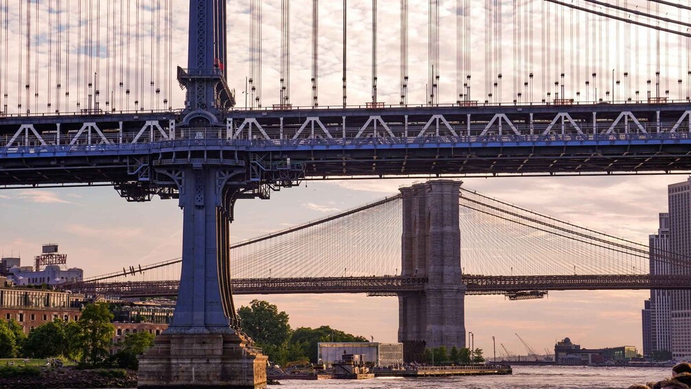 Un puente colgante con cables y torres, un río abajo y edificios de la ciudad al fondo. 2
