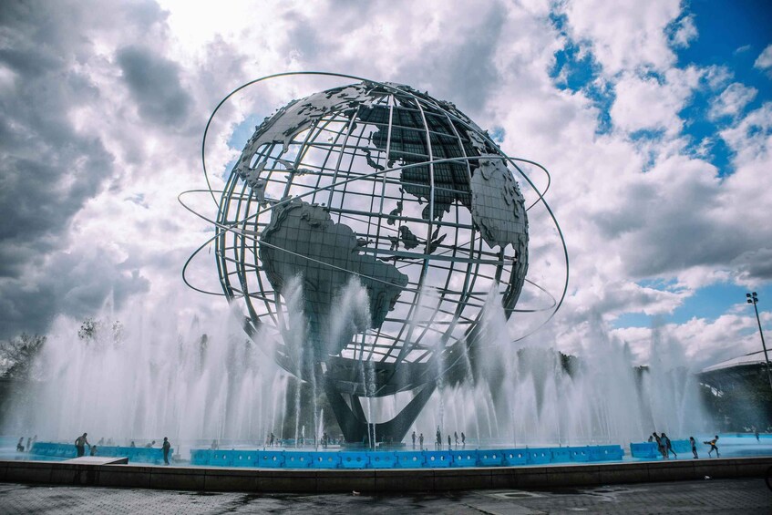 Una gran escultura de un globo rodeado de fuentes de agua, con un cielo nublado de fondo. 5