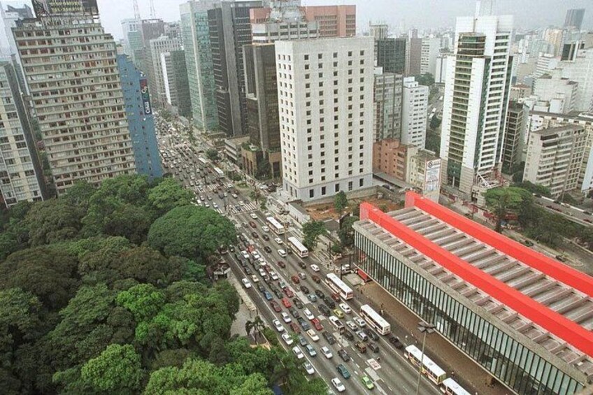 A busy urban street with tall buildings, dense traffic, and a large green park area. 3