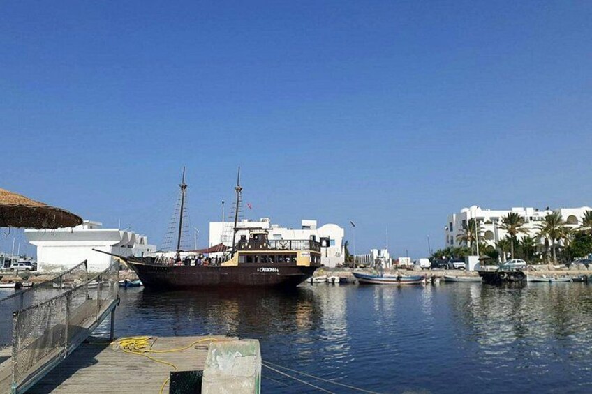 A harbor with a large boat docked, a pier, and buildings in the background. 3