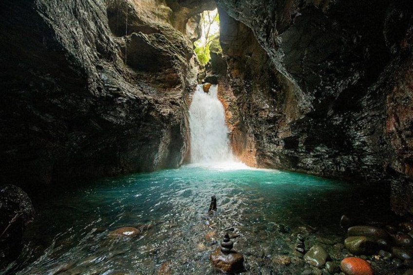 Een grot met een waterval, helder water en rotsen. 5