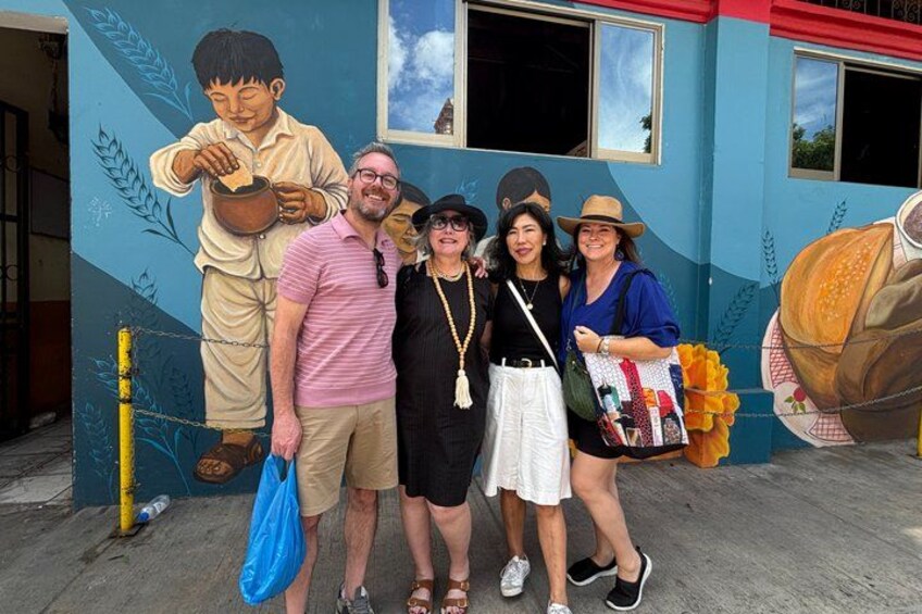 A mural with a boy holding a pot, a building with windows, and a person carrying a bag. 1
