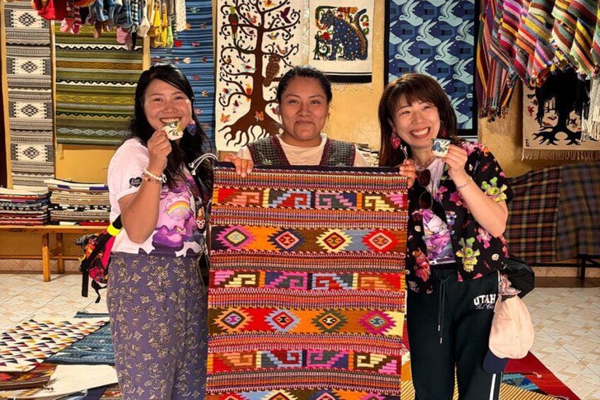 Three people holding a colorful woven textile. 2