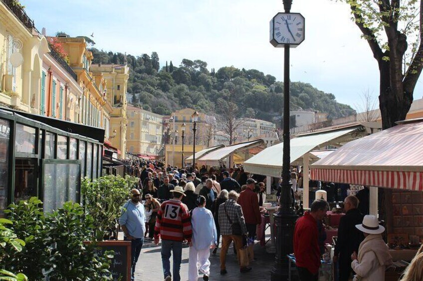 A crowded street with people walking, shops, and a clock on a pole. 5