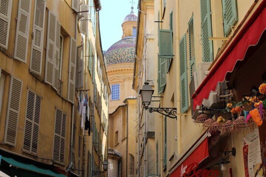 A narrow street with buildings, a dome, and hanging laundry. 4
