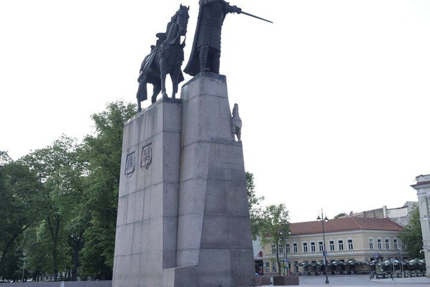 A statue of a mounted figure with a sword, set against a backdrop of trees and buildings. 2