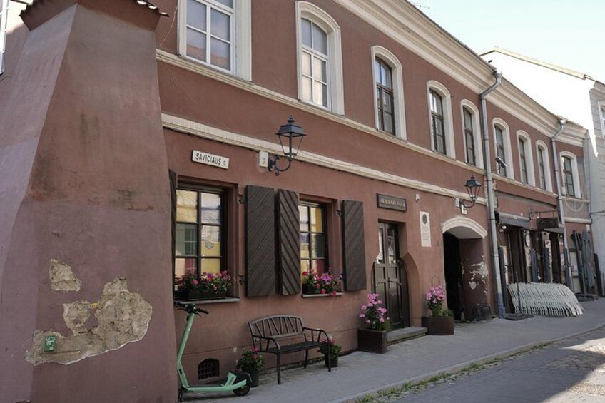 A building with a sign reading 'SANVICCIUS,' a bench, a scooter, and potted plants. 3