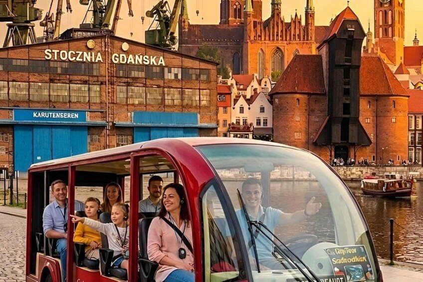 A red tour bus with passengers, a historic building, and a river in the background. 1