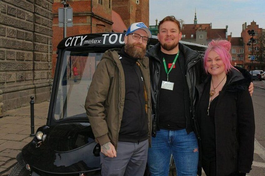 Three people standing in front of a black vehicle with 'CITY melex TOUR' on the windshield. 3
