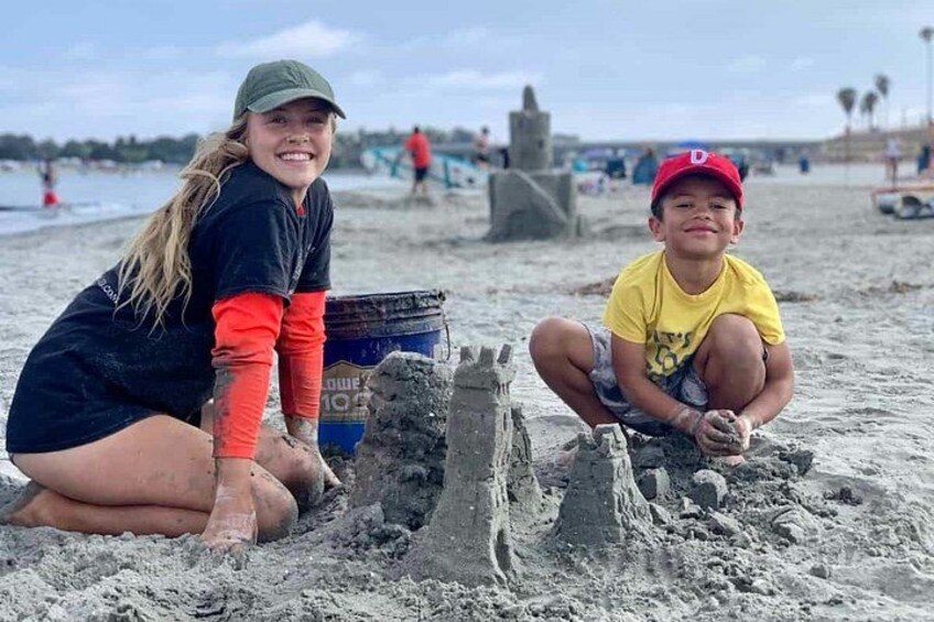 Two children building a sandcastle on a beach with a blue bucket in the background. 1
