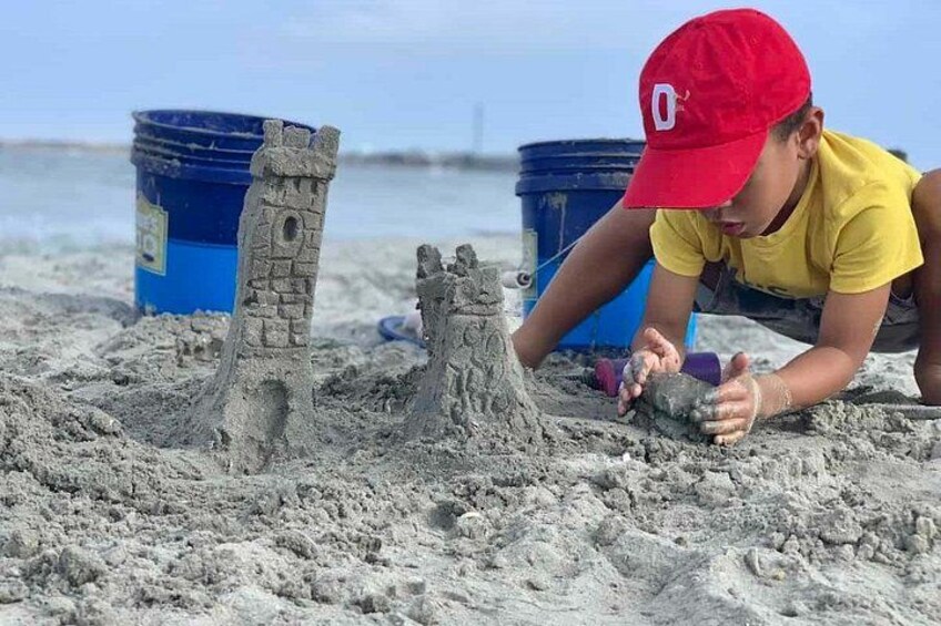 A person building a sandcastle on a beach with blue buckets in the background. 5