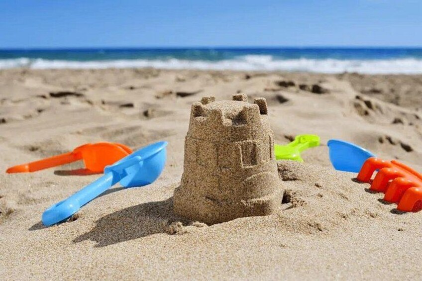 A sandcastle on a beach with a blue shovel, an orange shovel, and a green shovel nearby. 2