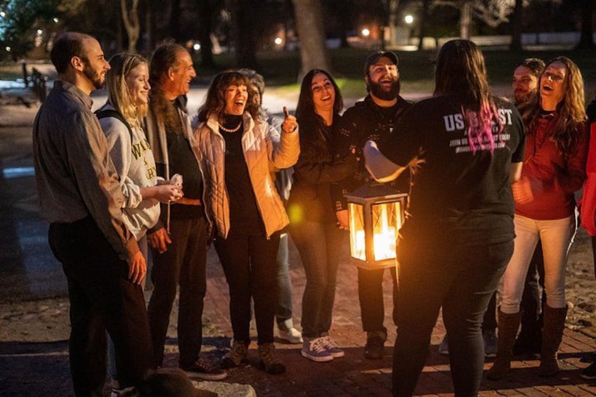 Un grupo de personas reunidas al aire libre de noche, algunas sosteniendo un farol. 4