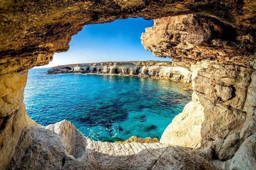 A coastal landscape with a natural rock arch, clear blue sea, and rocky cliffs. 3