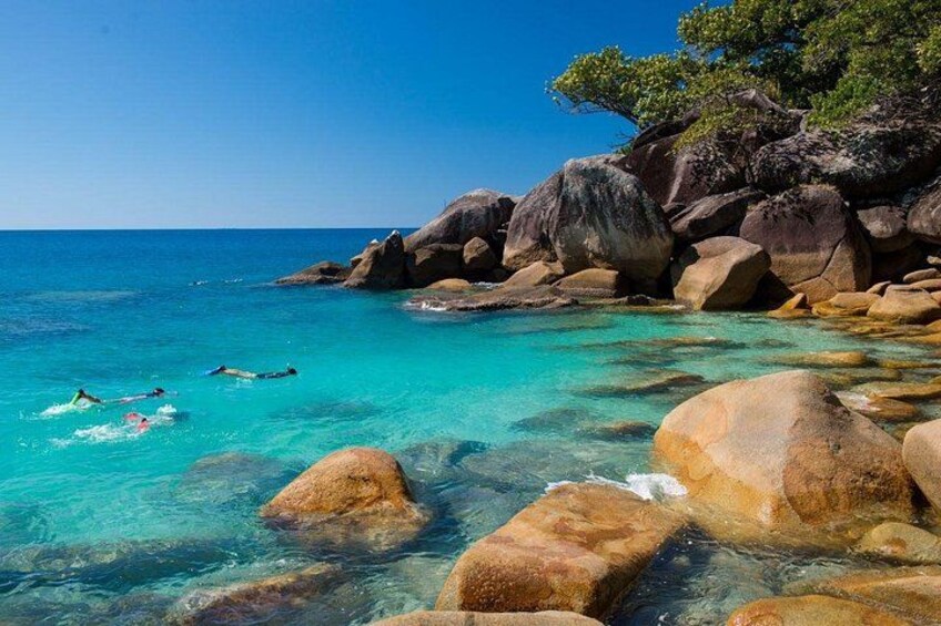 Une mer turquoise aux eaux limpides, de gros rochers et quelques personnes qui se baignent. 5