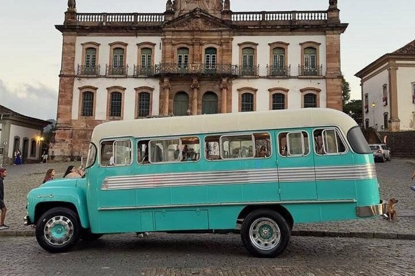 A turquoise vintage bus parked in front of a historic building with columns and a balcony. 3