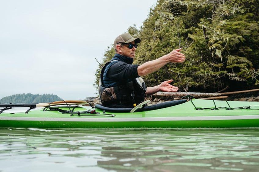 A person in a green kayak on calm water, pointing towards the shore. 5