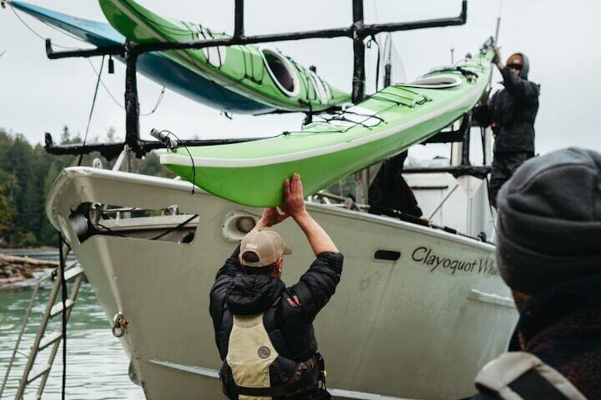 A person handling a green kayak on a boat named Clayquot Wall. 4