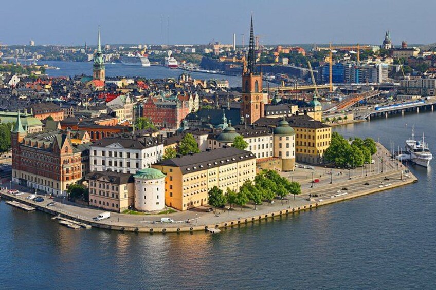 En stadsbild vid en flod med historiska byggnader, ett framträdande kyrktorn och en bro i bakgrunden. 4