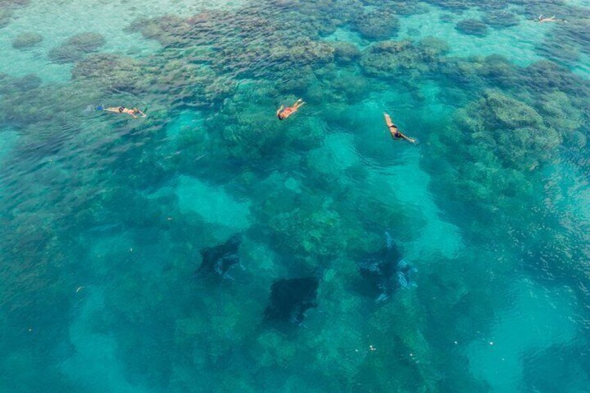 An aerial view of clear turquoise waters with visible coral reefs and people swimming. 2