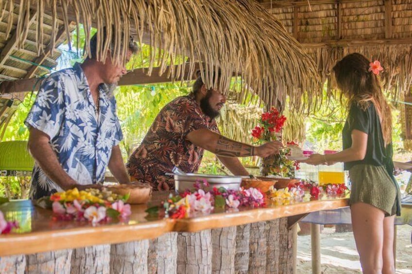 A tropical outdoor setting with a thatched roof, a wooden table adorned with flowers, and people engaged in a transaction. 4