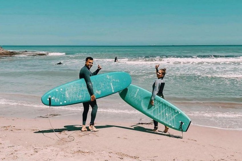 Deux personnes tenant des planches de surf sur une plage, avec des vagues en arrière-plan. 1