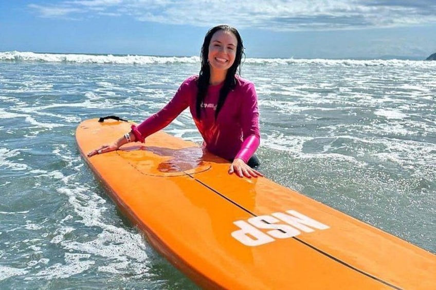 Une personne vêtue d’une combinaison de plongée rose, tenant une planche de surf dans l’océan. 3